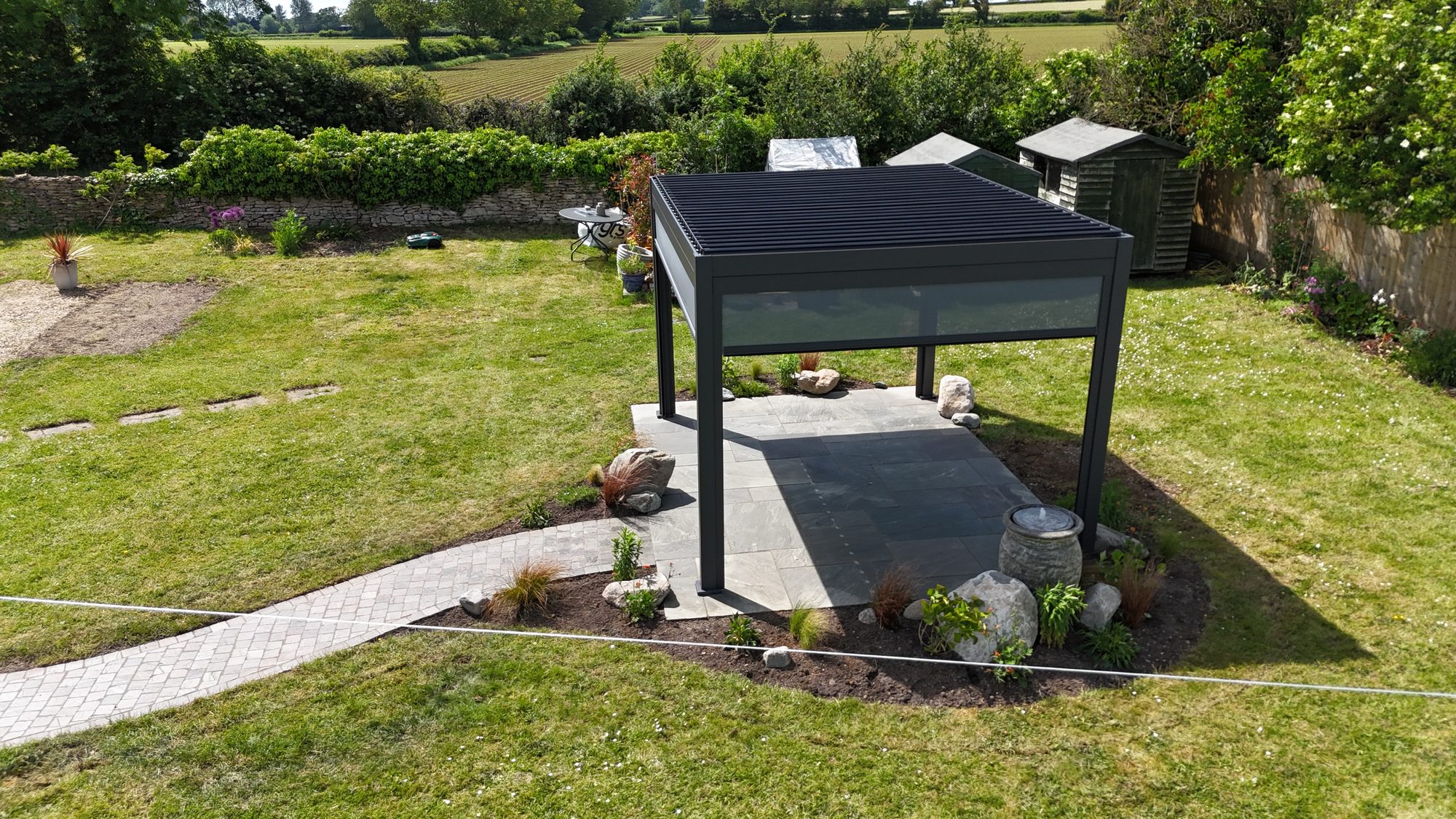 Aluminium louvred pergola with a curved cobbled path and planting, aerial view