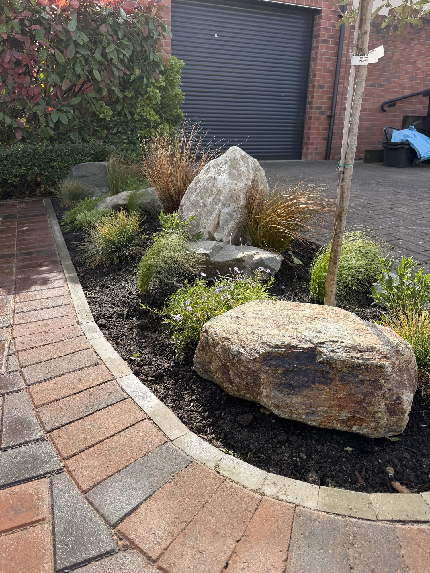 Planting island detail with boulders and ornamental grasses beside block paving