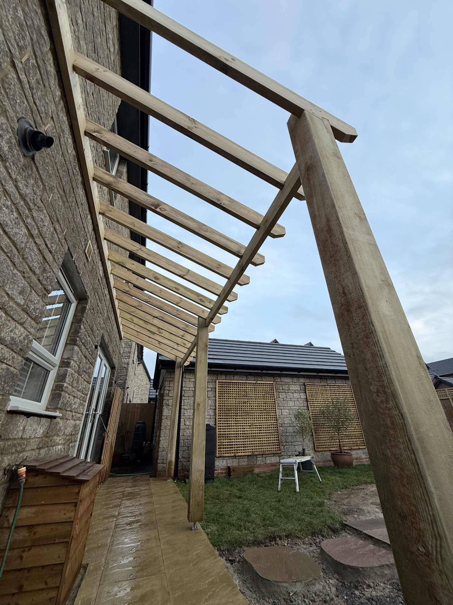 Timber lean-to pergola built against a stone house over a porcelain patio