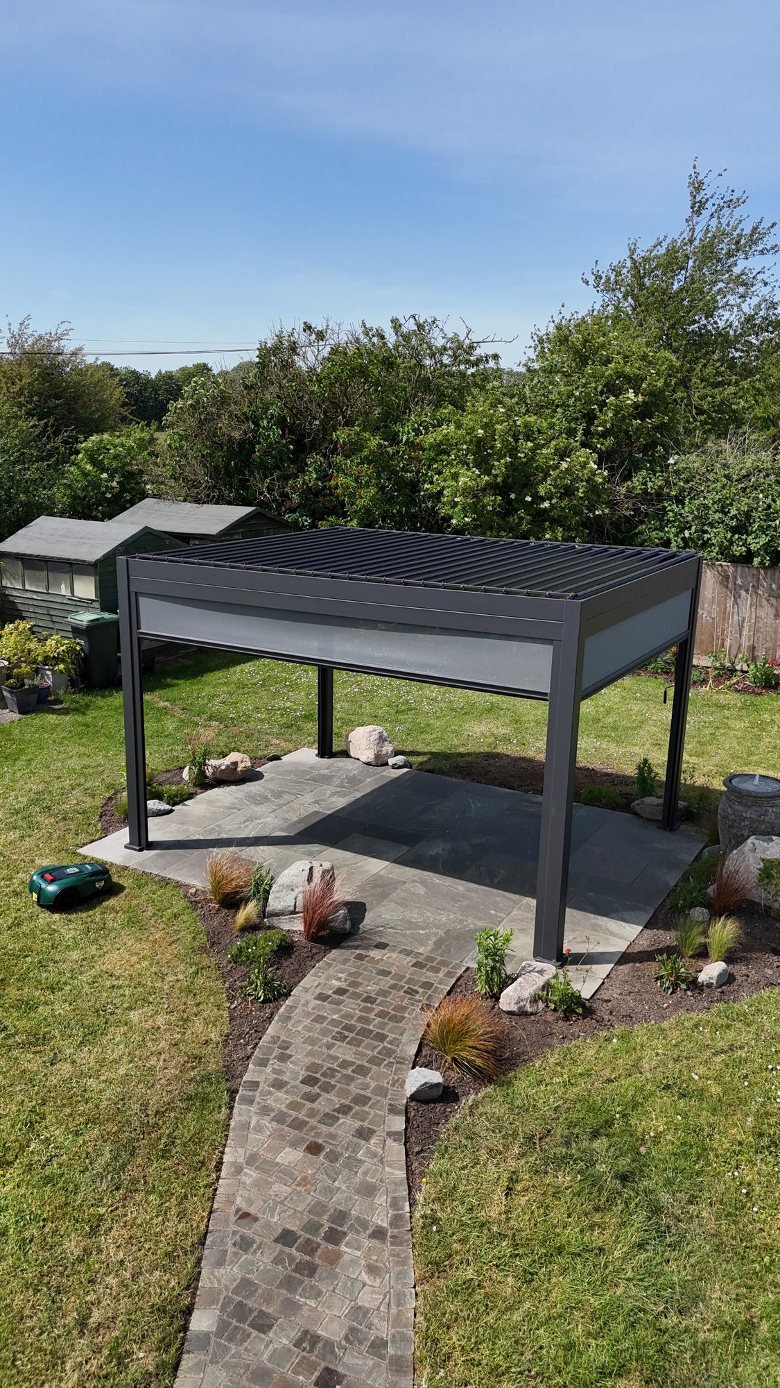 Louvred pergola with a curved cobbled path winding through planting