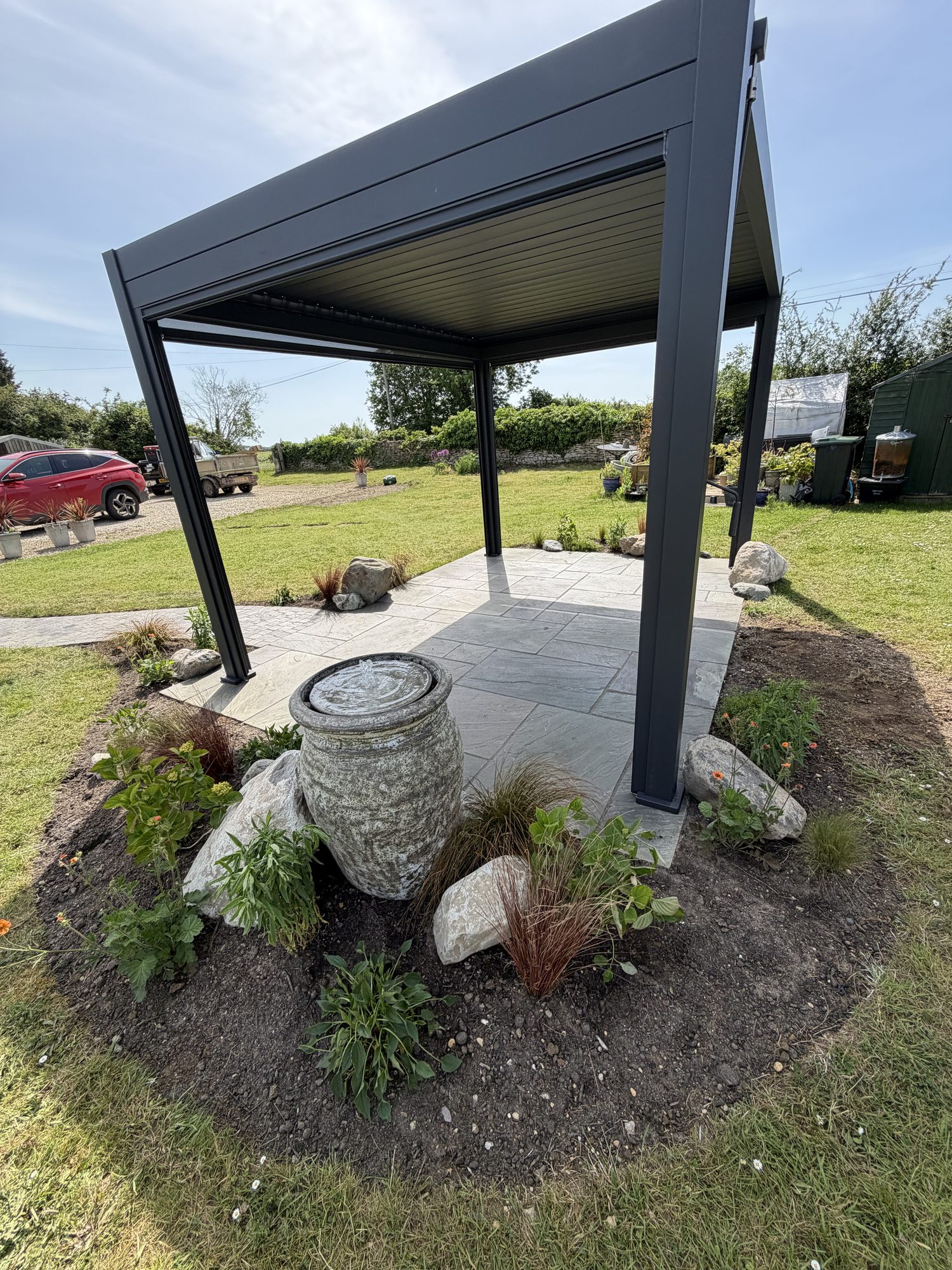 Louvred pergola beside a stone urn water feature on a sandstone patio