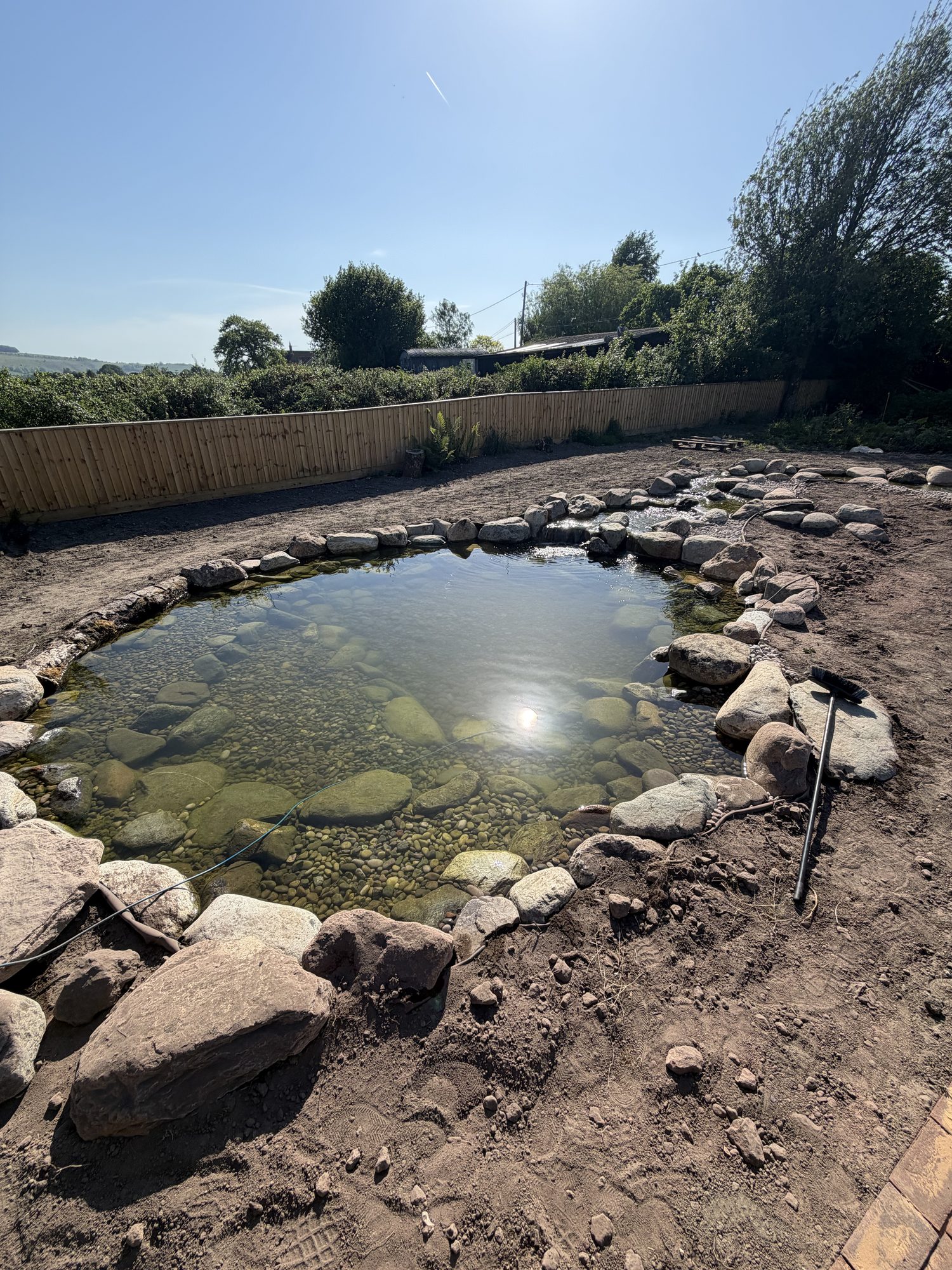 Newly built natural wildlife pond with boulder edging and a clear pebble base