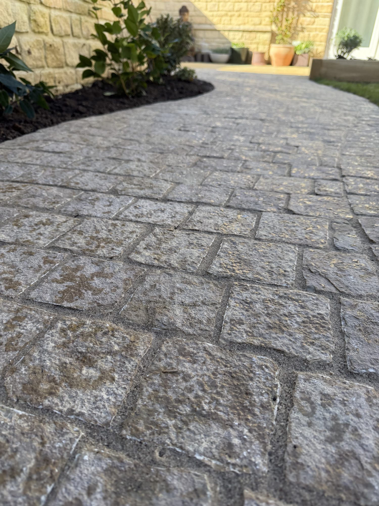 Low-angle detail of a tumbled cobble-sett path beside Cotswold stone walls and terracotta pots